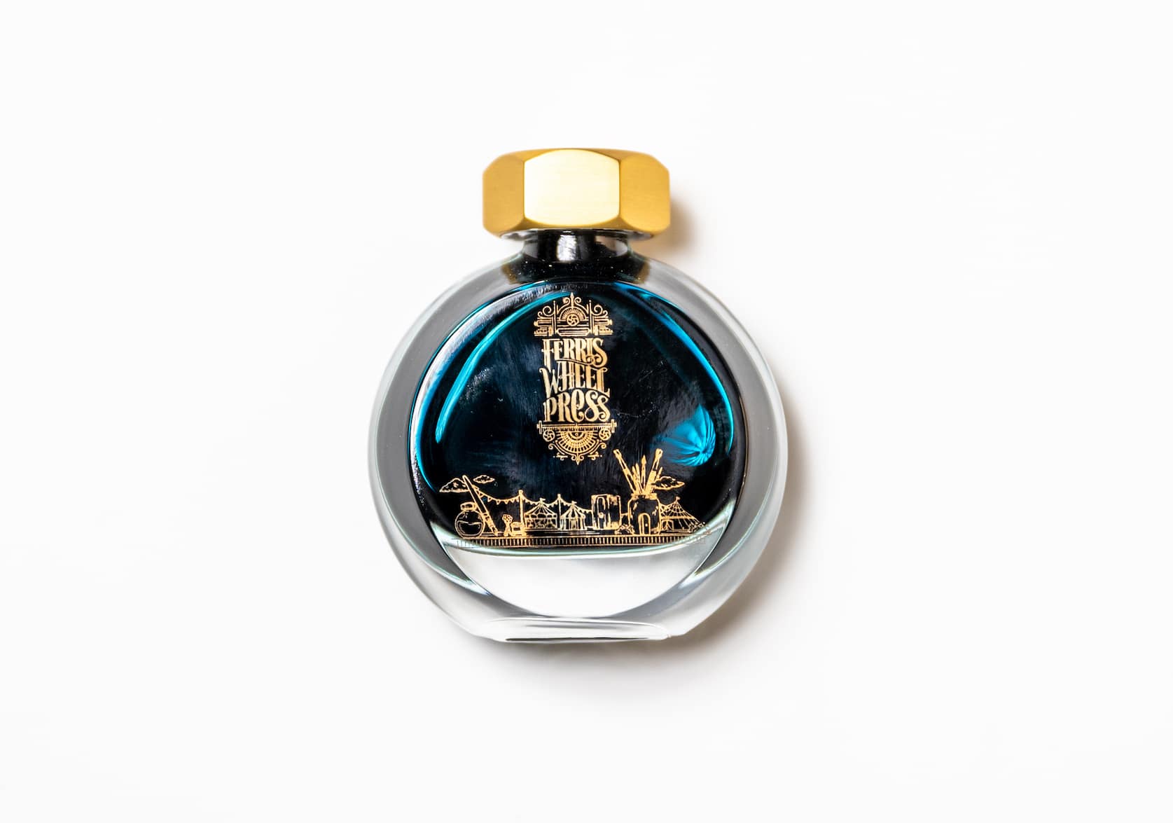 A round glass bottle of ink with a gold lid. On the bottle there is a small gold illustration featuring a merry-go-round and circus tent.