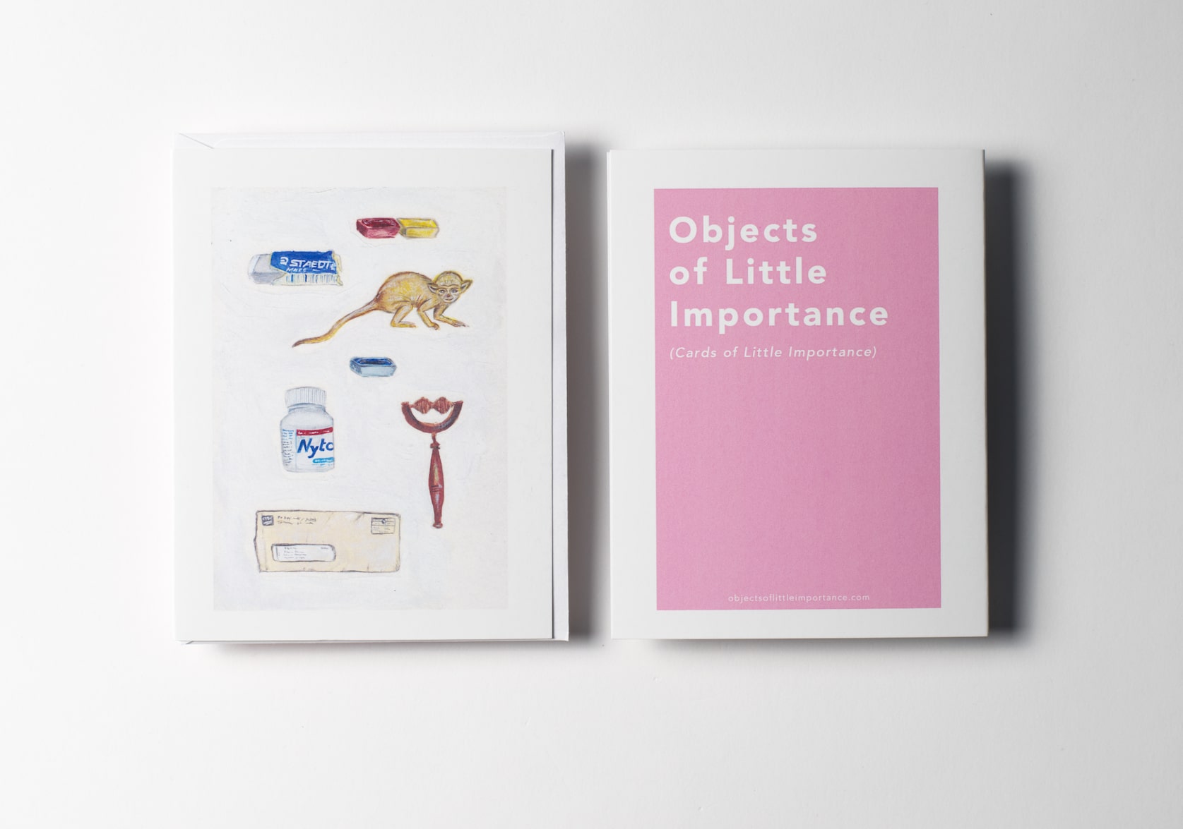 White greeting card featuring paintings of a set of watercolors, a used Staedtler eraser a rubber monkey toy, a bottle of Nytol sleeping pills, a wooden neck massage roller, and an envelope with Visa statement. Back of the card is a pink rectangle with white text that reads: Objects of Little Importance (Cards of Little Importance).