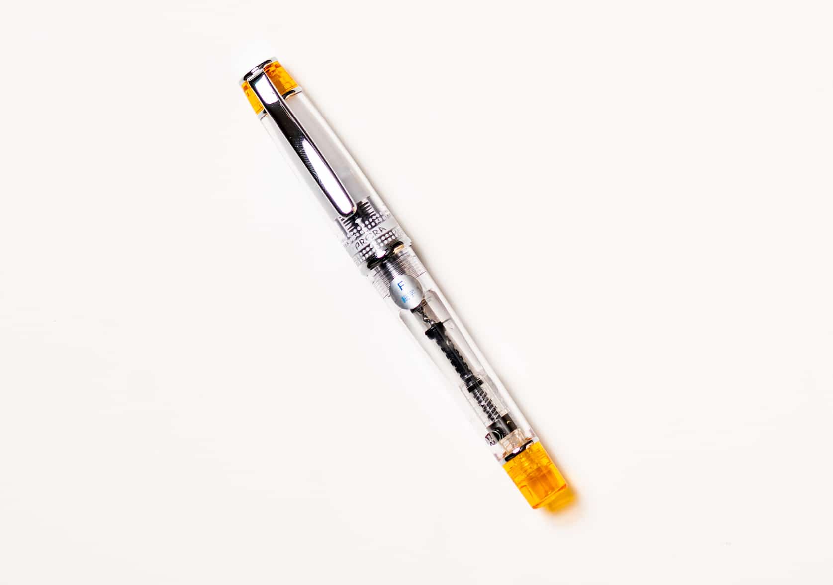 Transparent fountain pen with silver pen clip. Tinted orange details on the top of the pen cap and bottom of the barrel