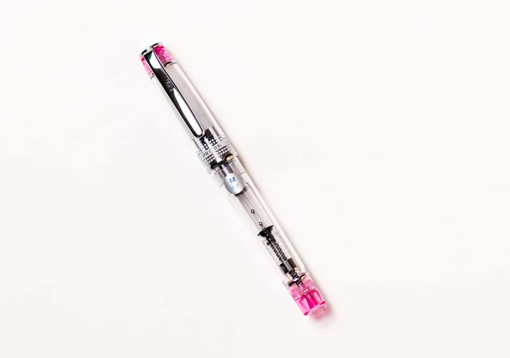 Transparent fountain pen with silver pen clip. Tinted pink details on the top of the pen cap and bottom of the barrel