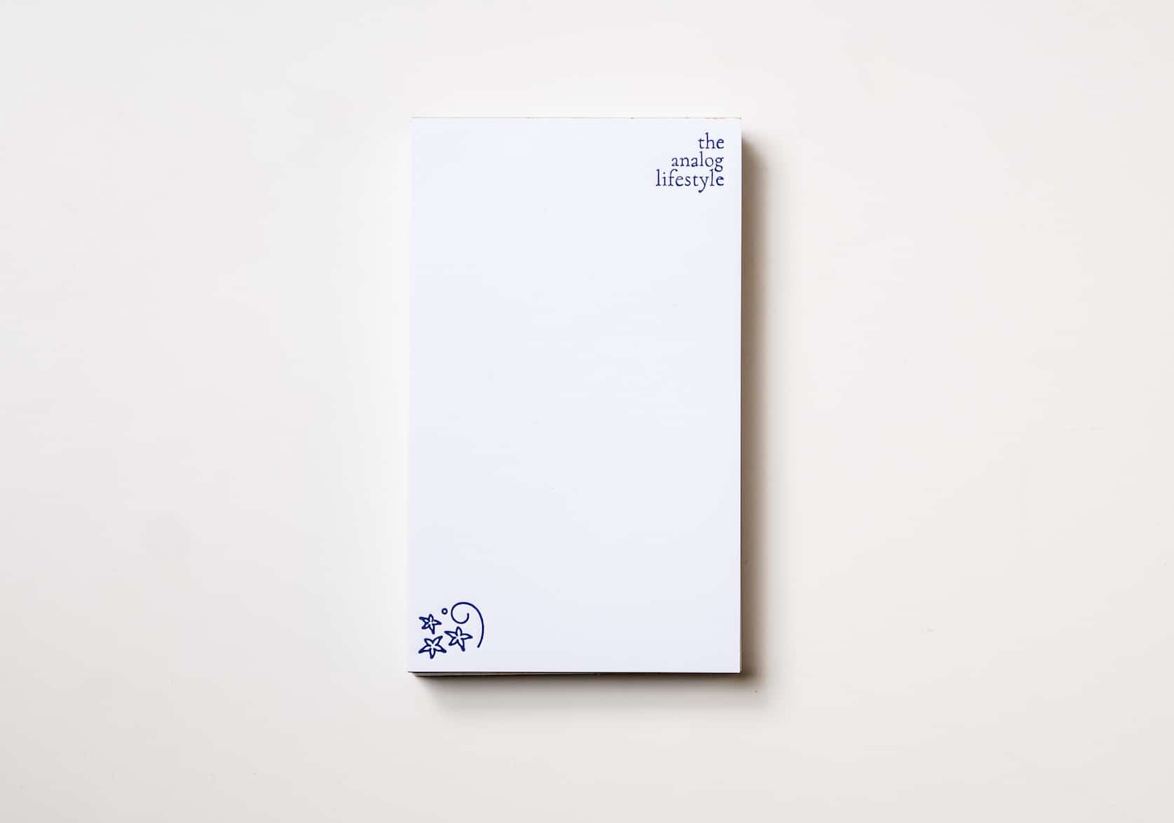 White notepad with text on the top right that reads: the analog lifestyle. A decorative stamp on the bottom left