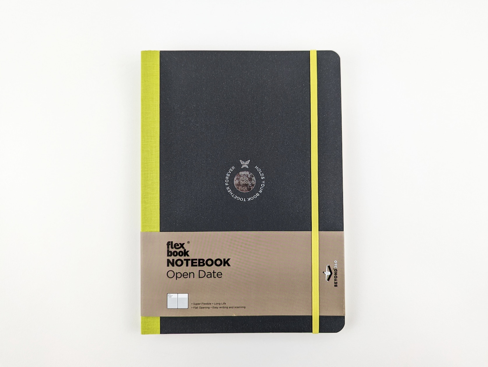 A black notebook with a light green fabric spine and elastic band closure. A circular holographic logo is featured in the center with a butterfly and silver text wrapping around that reads: Holds your book together forever. Light brown paper packaging is located across the bottom half of the notebook with black text that reads: flexbook Notebook Open Date. Super Flexible. Long Life. Flat Opening. Easy Writing and Scanning. Beyond 360.