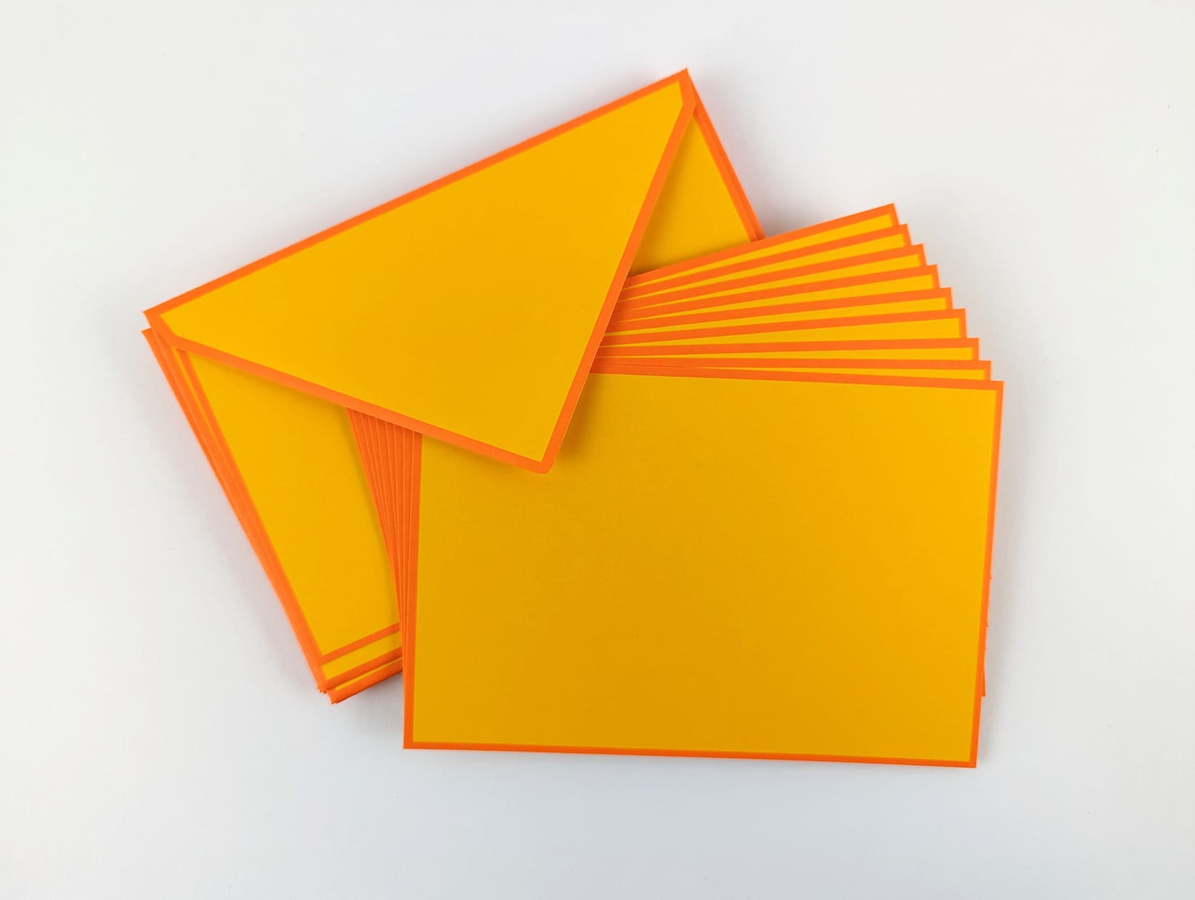 Arranged stack of bright mango Flat Note Cards and matching envelopes with orange border