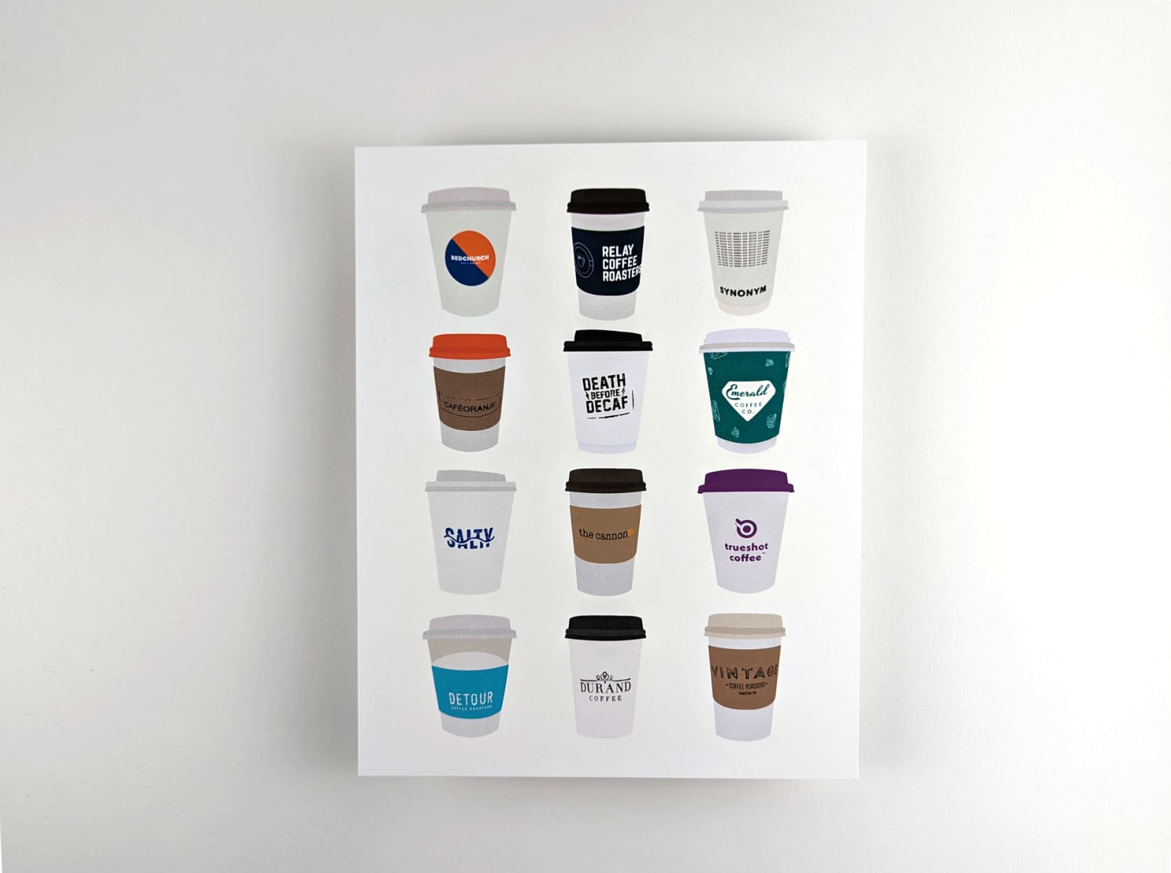 Print featuring illustrations of twelve coffee to-go cups from Hamilton cafés against a white background. The twelve coffee cups are arranged in 4 rows with 3 cups in each row.