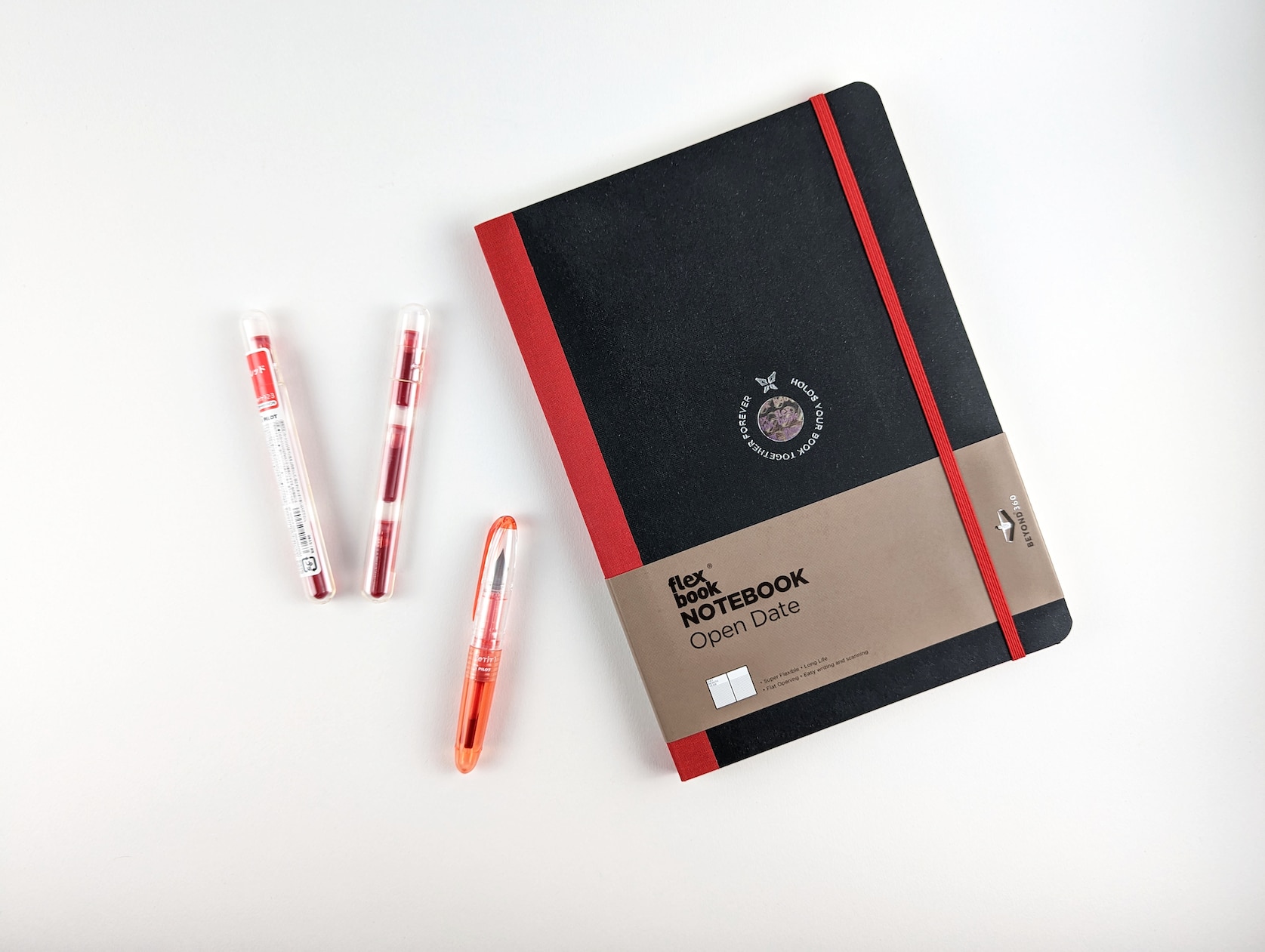 Bundle of items on a white background. Items include: red & black notebook, red fountain pen and two pack of fountain pen ink cartridges.