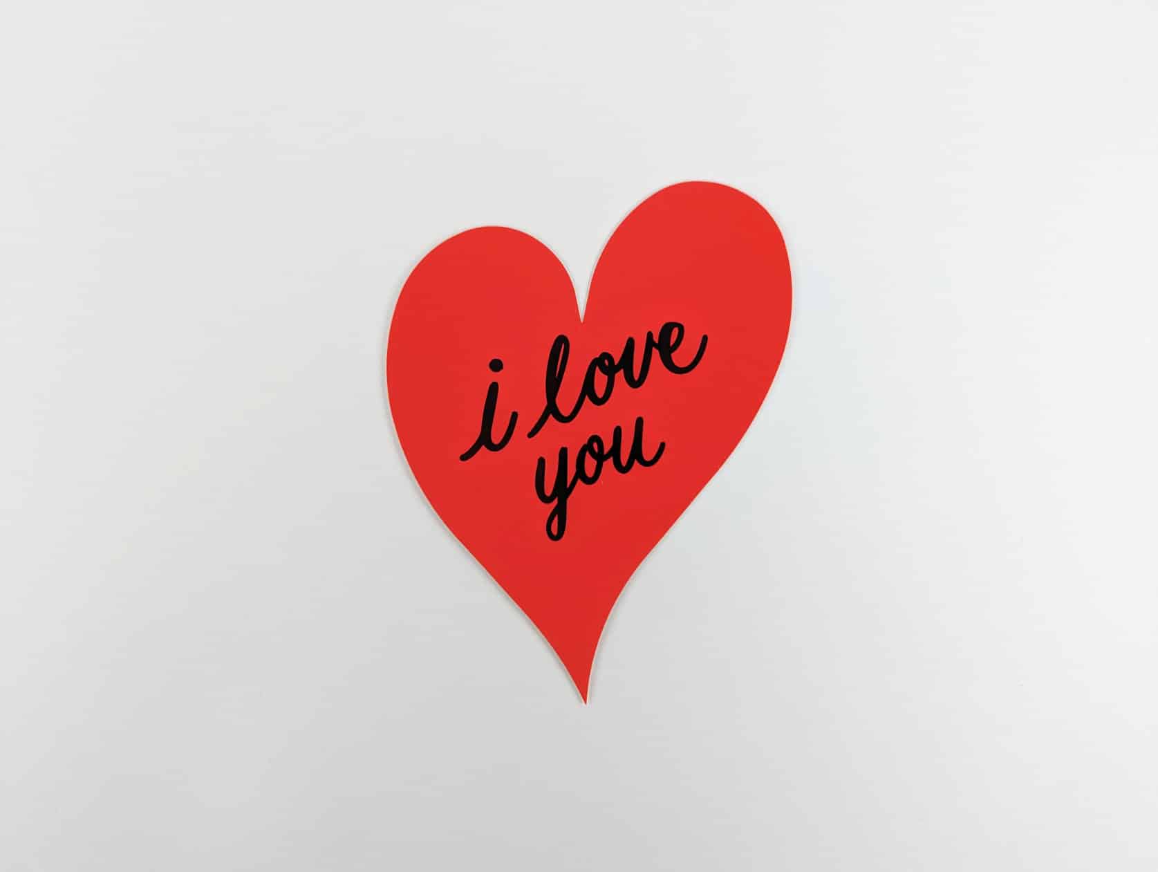 Red heart shaped card with a black cursive text in the centre that reads: i love you.