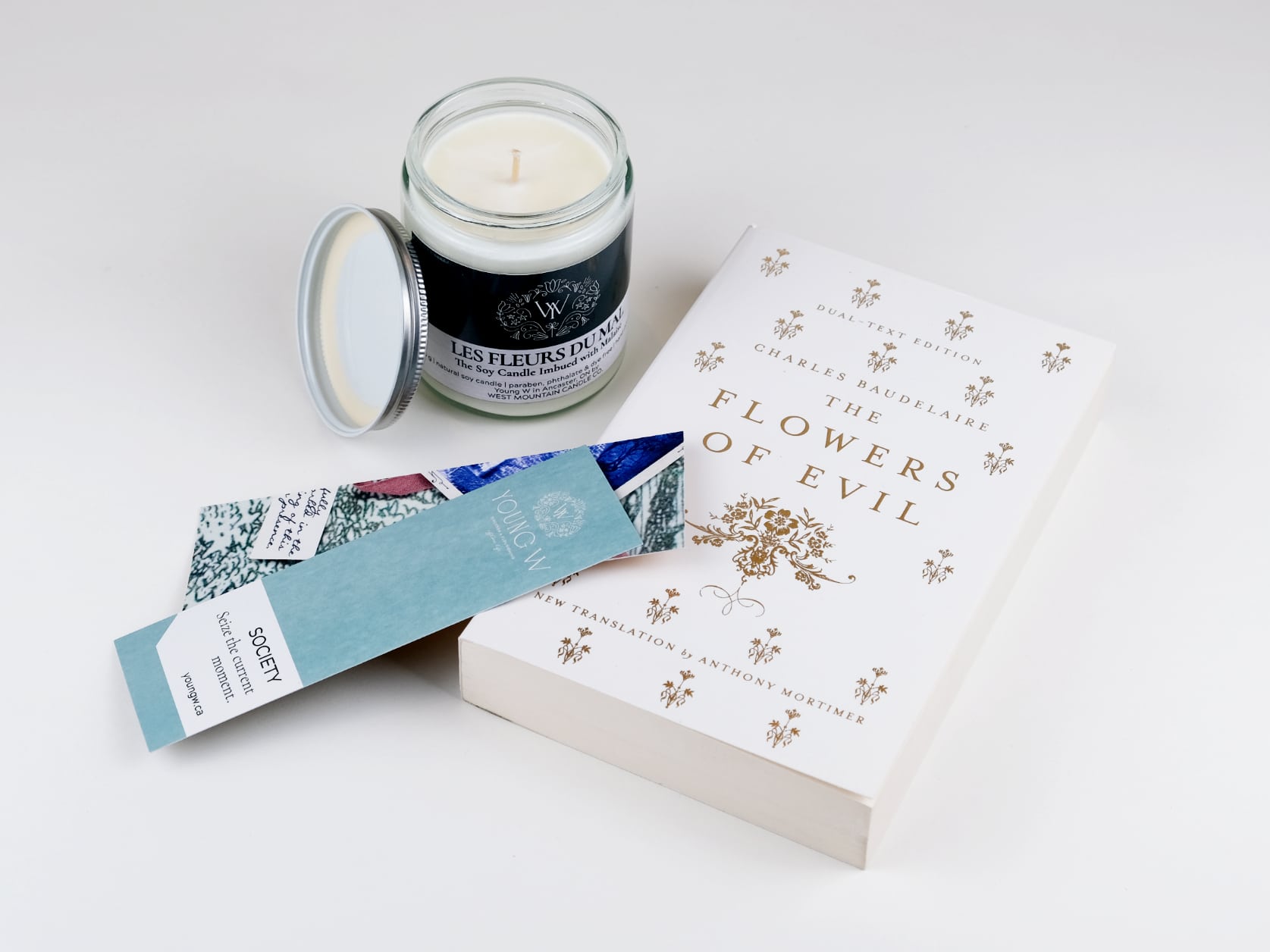 Two Young W bookmarks lying on top of the novel The flowers of evil which lies beside a les fleurs du mal scented candle