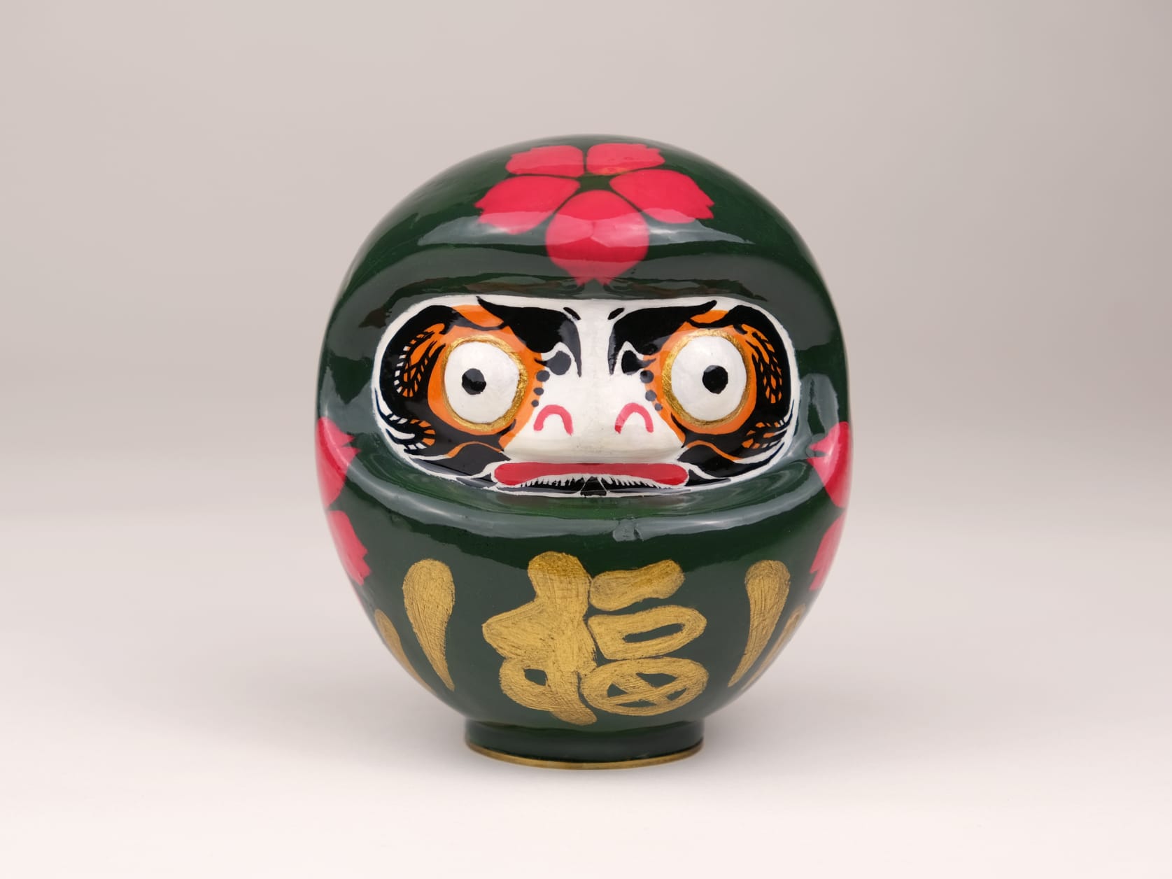 a sculpture of a dark green Daruma covered in bright pink cherry blossoms