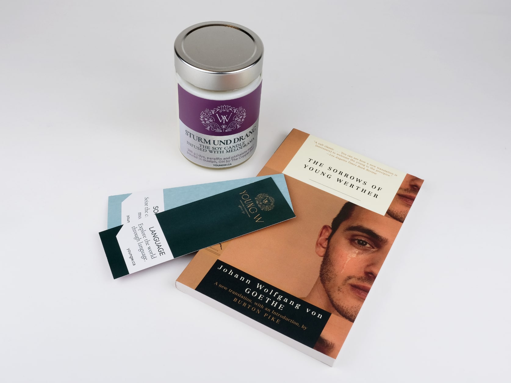 Two Young W bookmarks lying on top of the novel The sorrows of Young Werther which lies beside a sturm und drang scented candle.